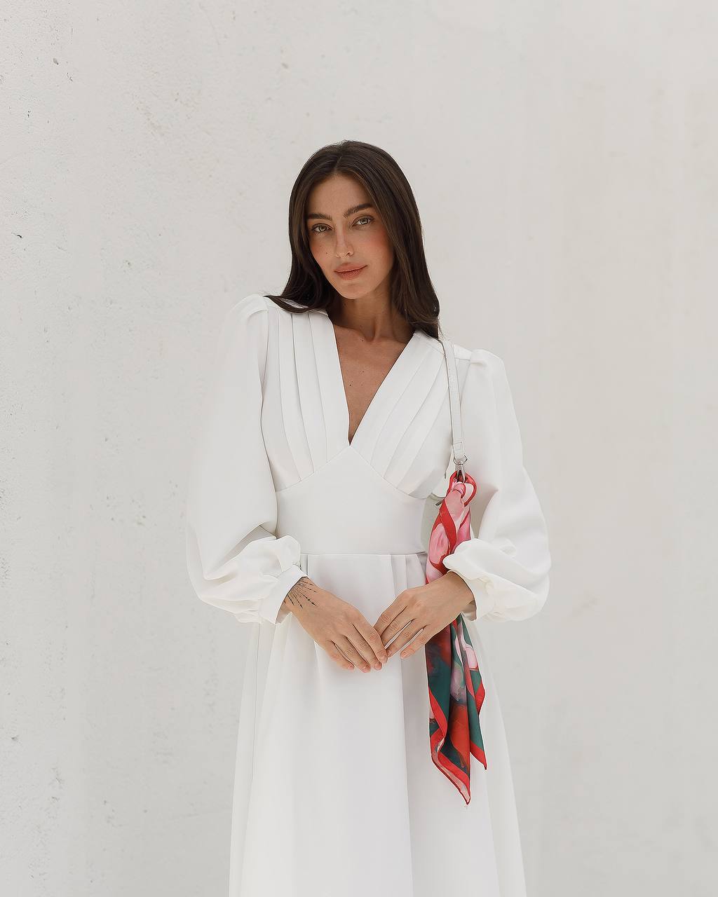 Woman wearing a white dress with a colorful scarf against a plain background