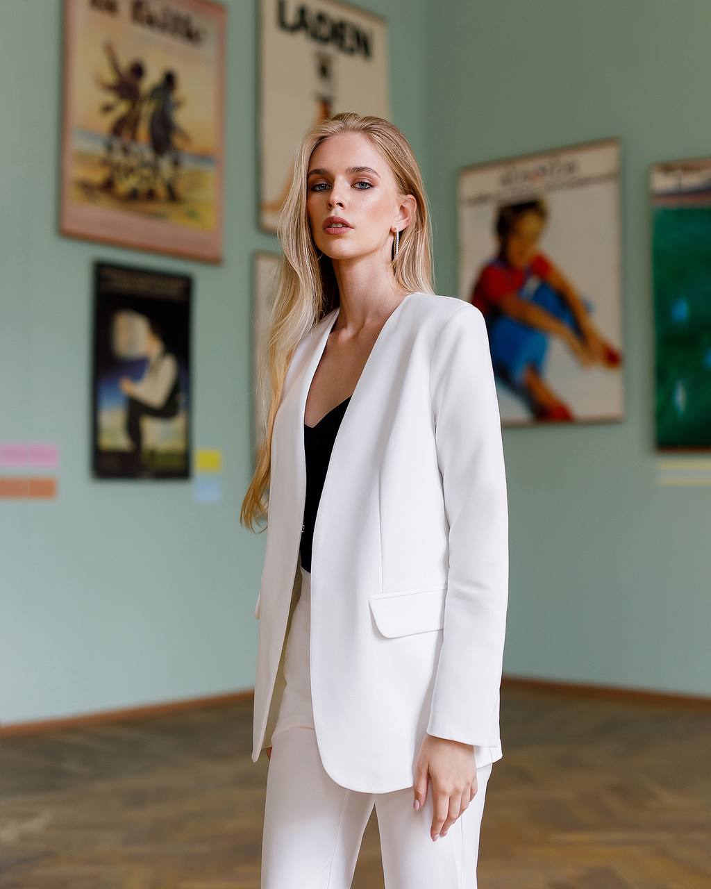 Woman in a white suit standing in an art gallery with posters on the wall.