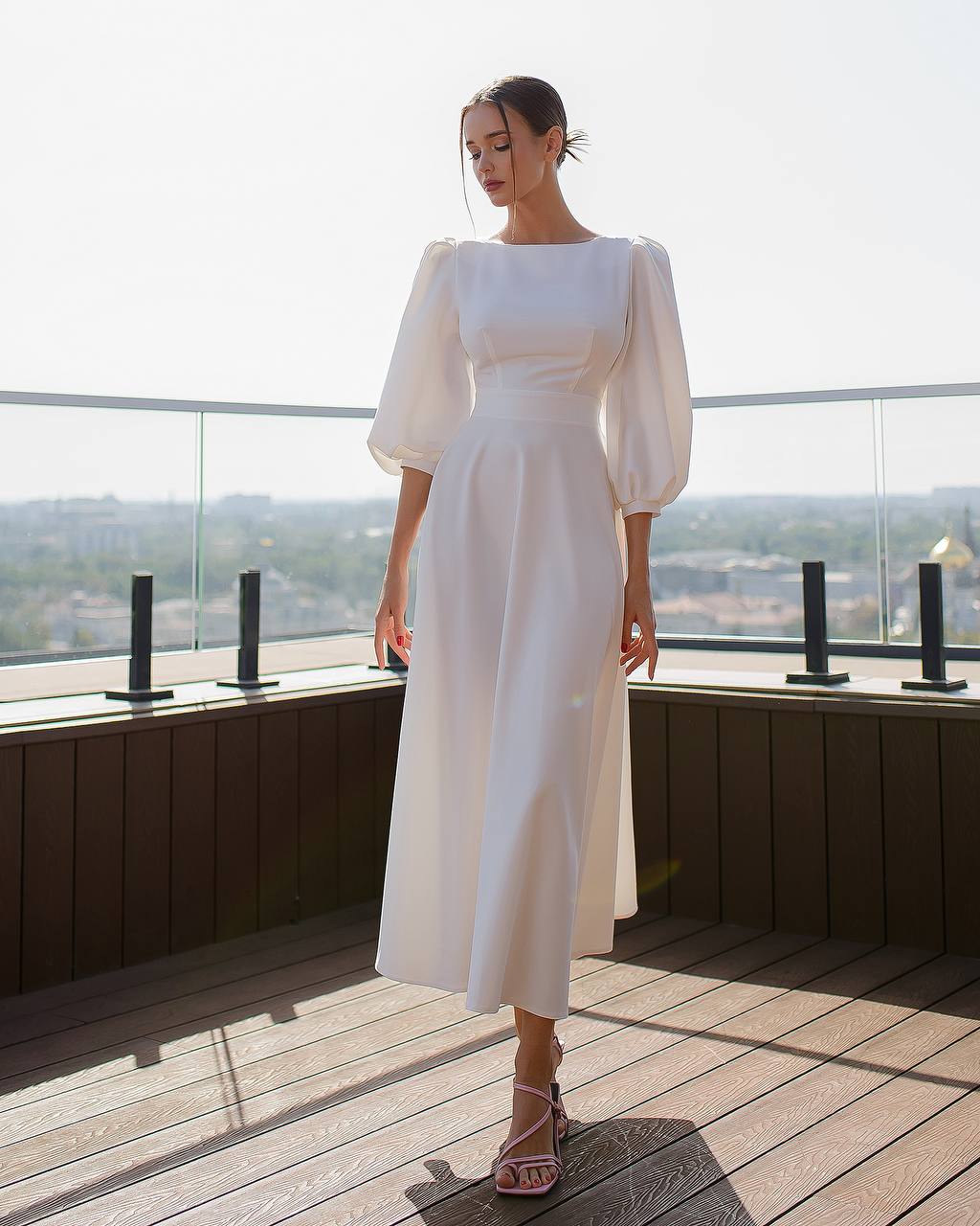 Woman in a white dress standing on a balcony with a scenic view.