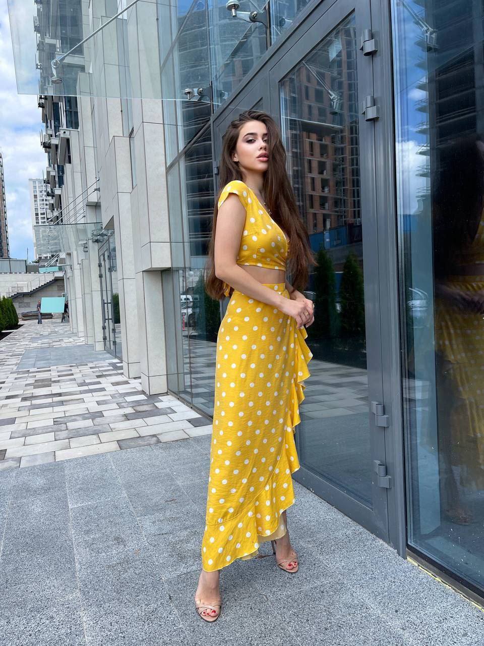 Woman in a yellow polka dot dress standing in front of a modern building.