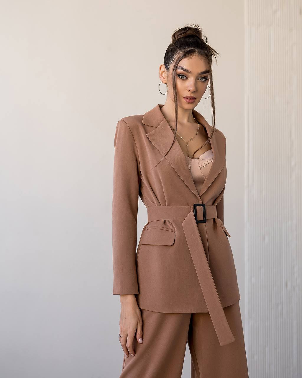 Woman wearing a brown suit with a belt against a neutral background