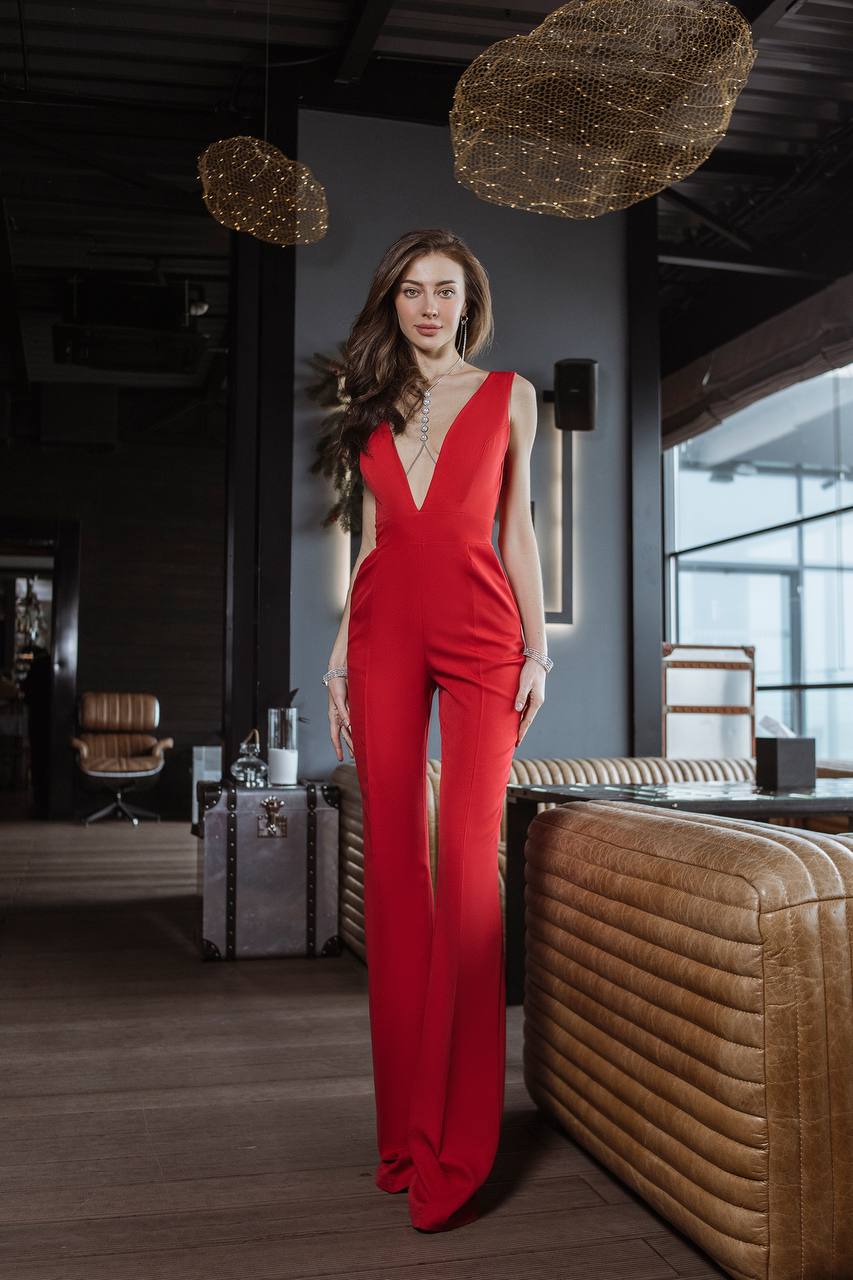Woman in a red jumpsuit standing in an elegant room with modern decor.