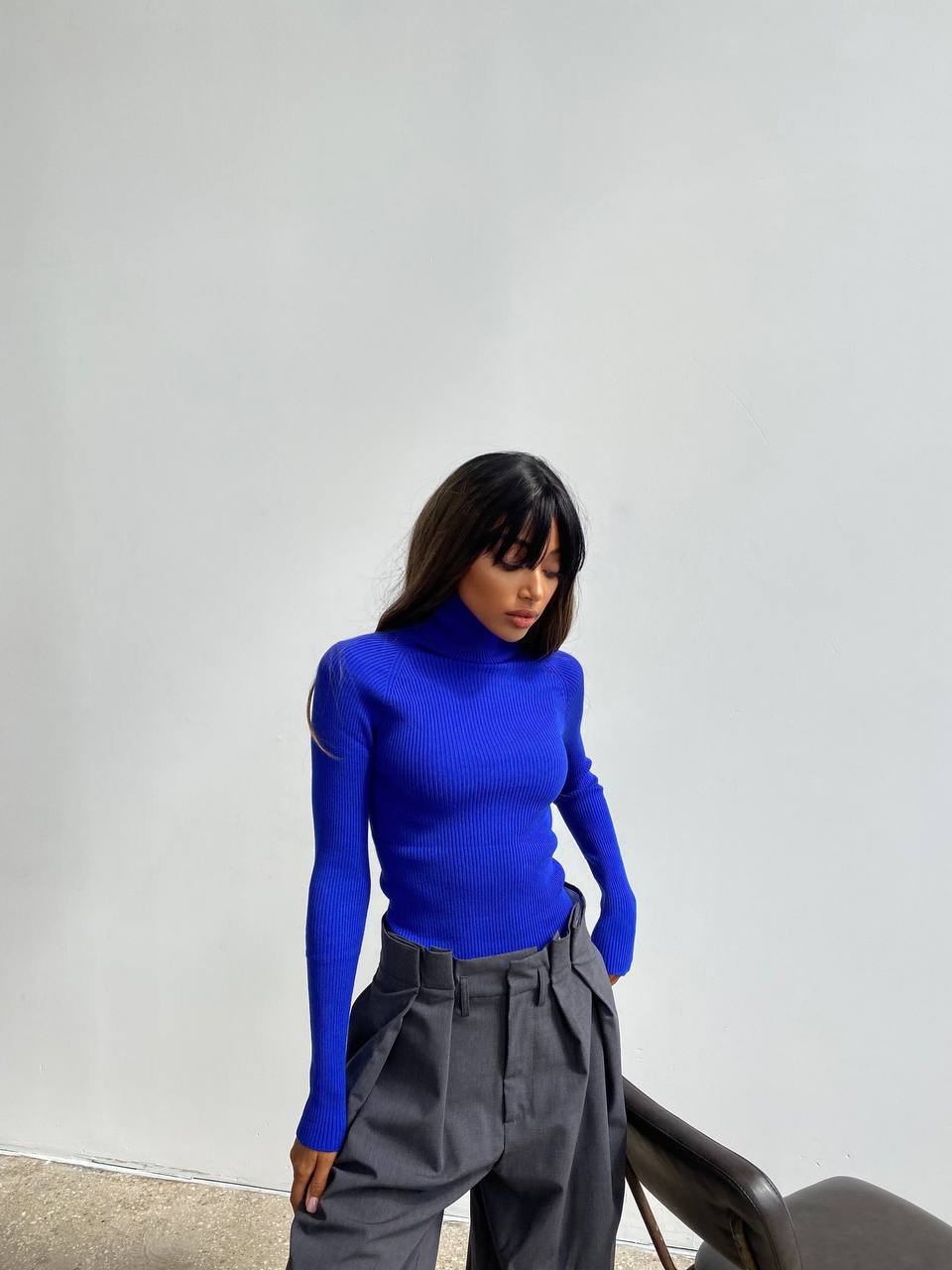 Person wearing a bright blue turtleneck and gray pants against a plain background