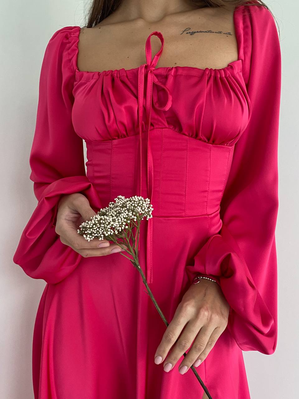 Person wearing a bright pink dress holding a small bouquet of flowers against a plain background