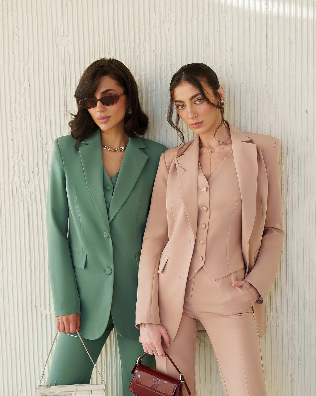 Two women in green and pink suits standing against a textured wall.
