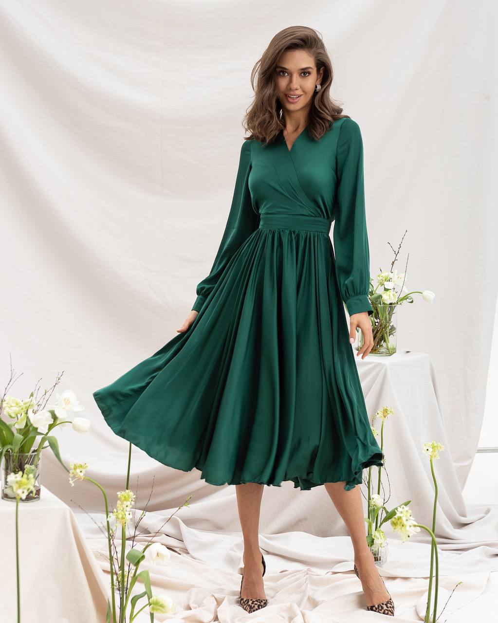 Woman wearing a green dress with long sleeves in a decorated indoor setting.