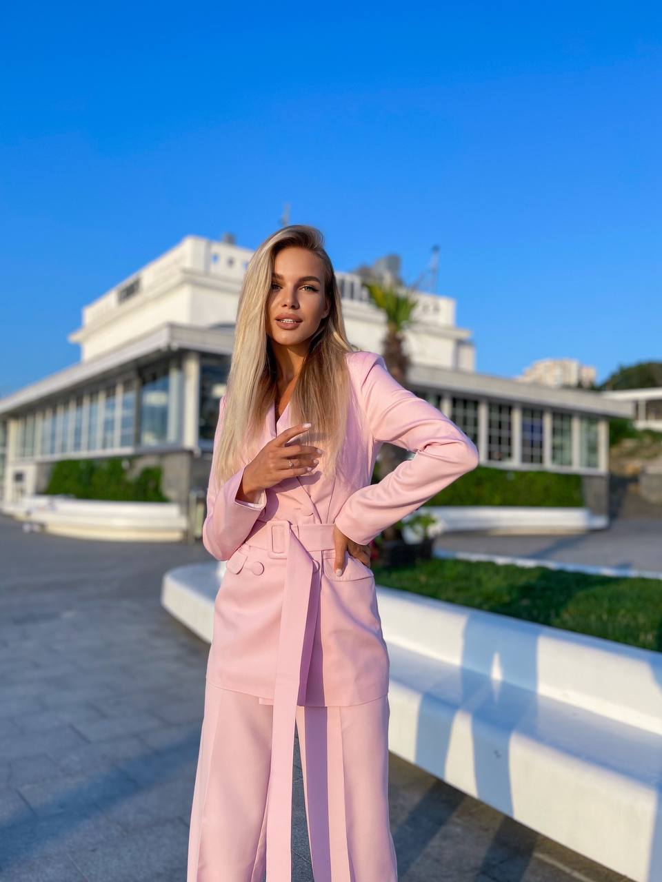 Woman in a pink suit standing outdoors with a building and blue sky in the background