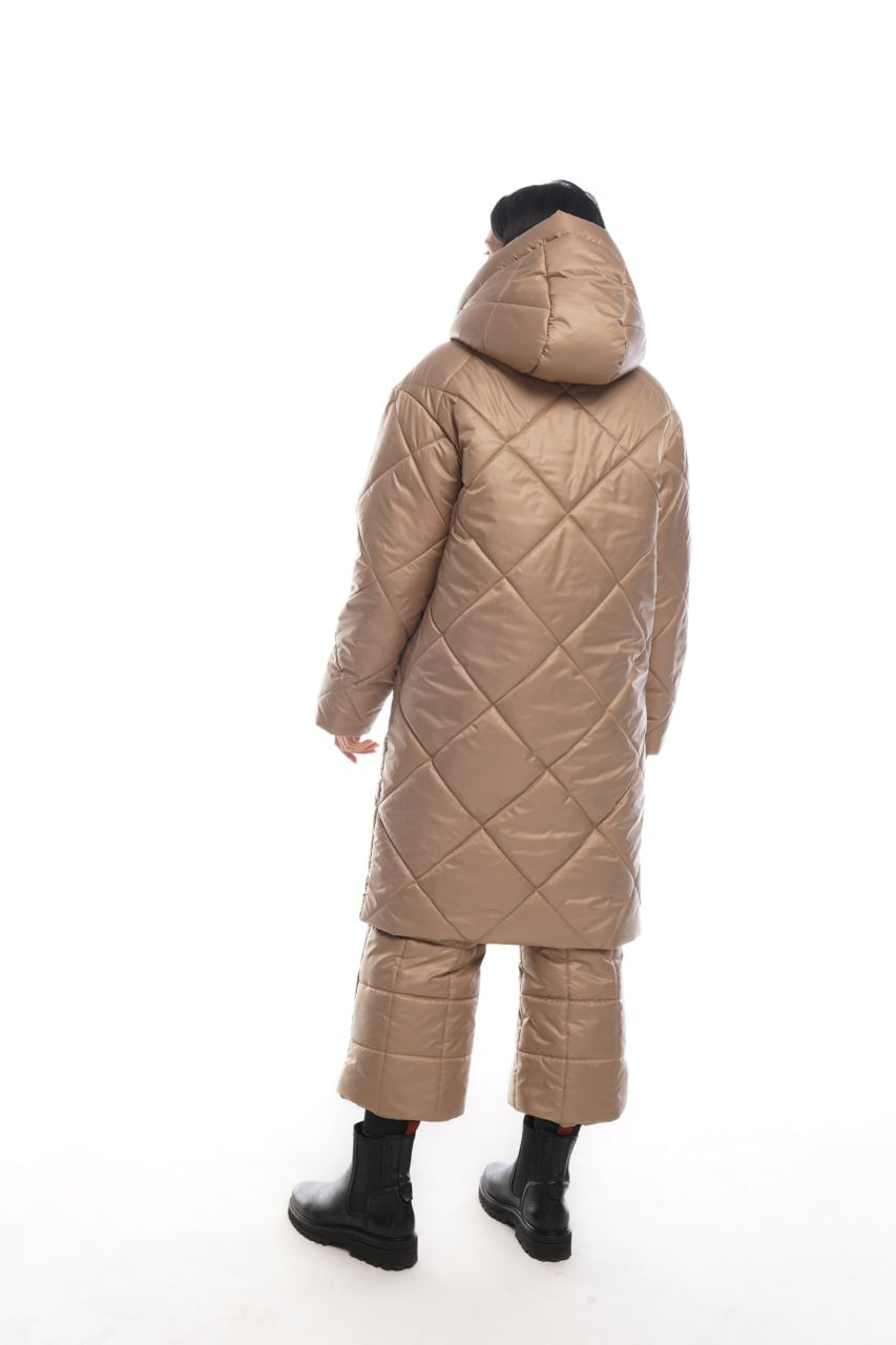 Person wearing a beige quilted coat and pants on a white background