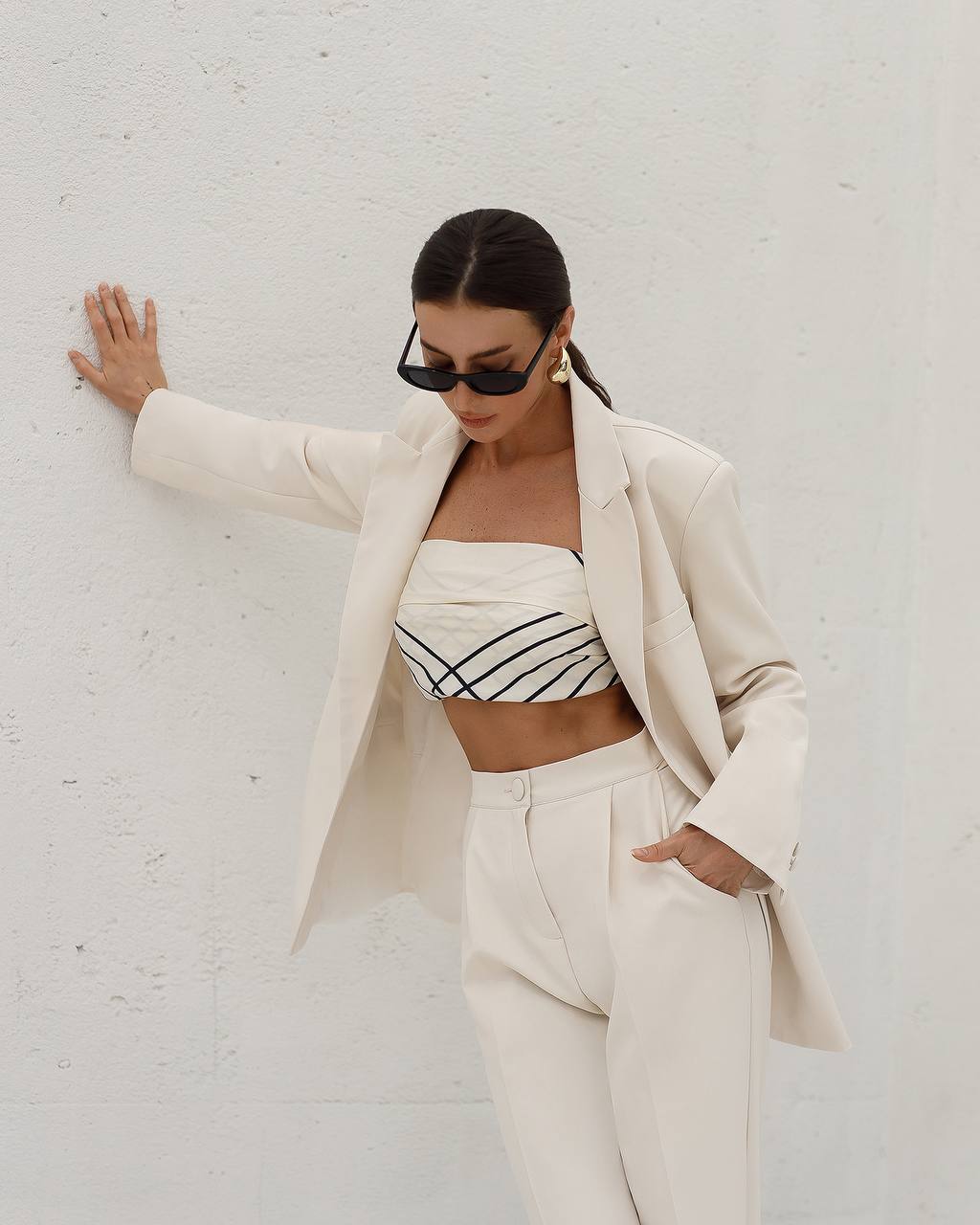 Woman in a stylish outfit with a white blazer and pants against a plain background
