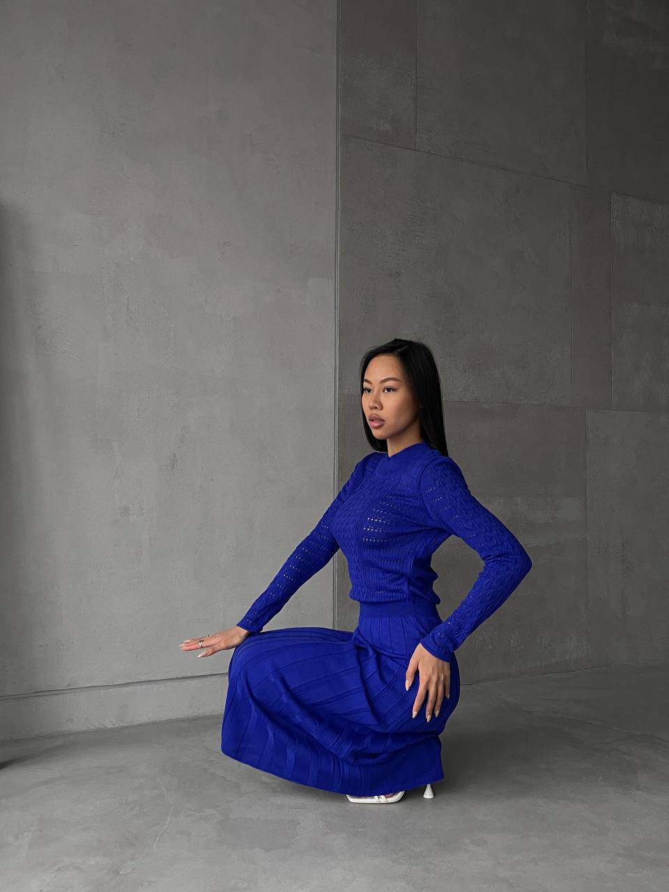 Woman in a blue dress posing against a gray wall