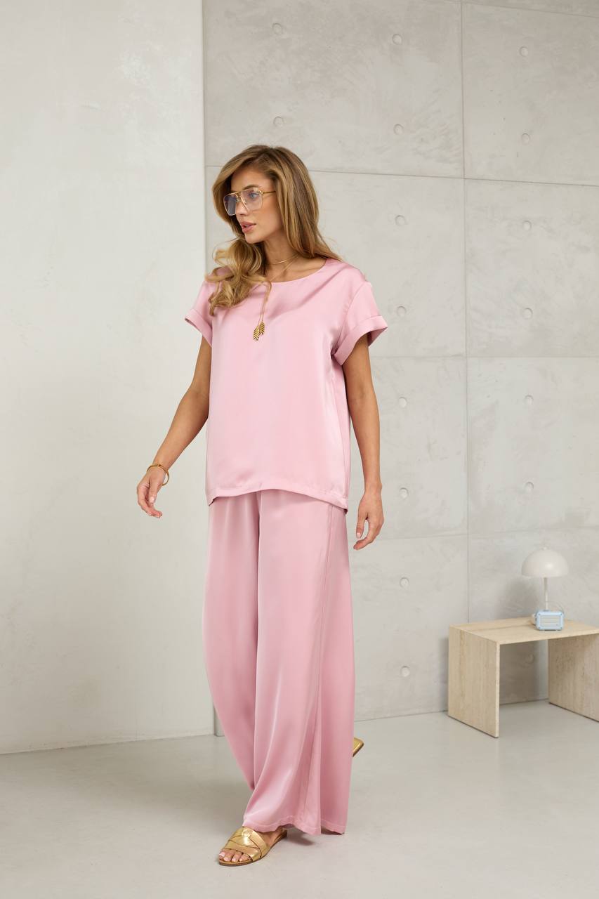 Woman wearing a pink outfit standing against a light gray wall.
