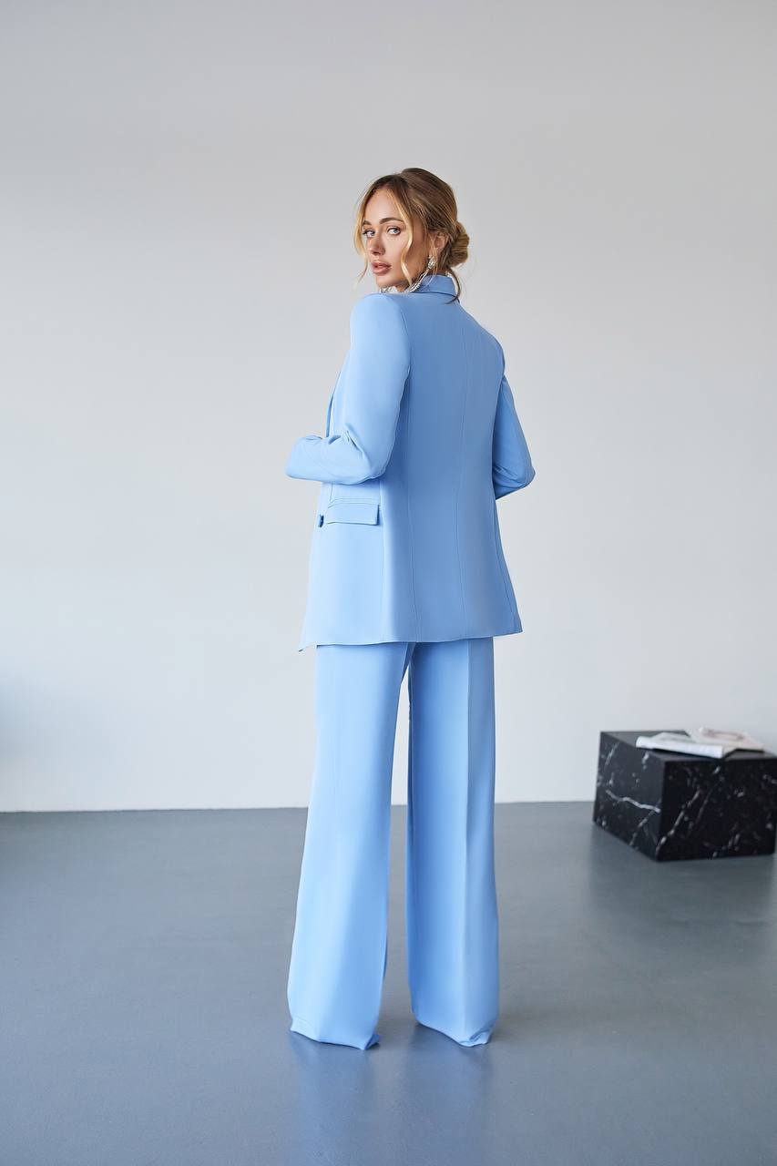Woman in a light blue suit standing in a minimalistic room with a black box on the floor.