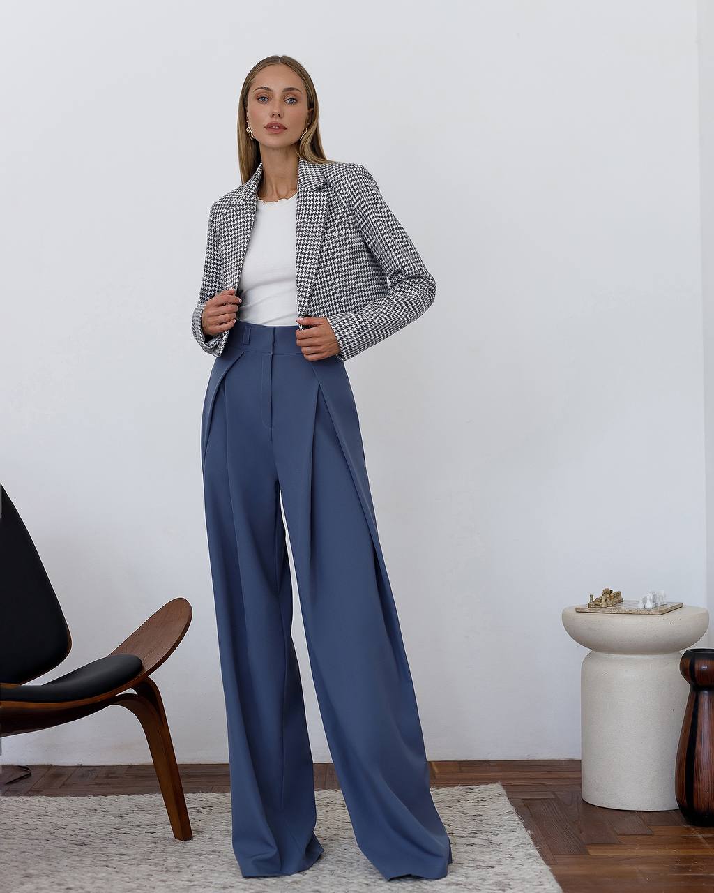 Woman wearing a checkered blazer and blue pants in a minimalistic room.