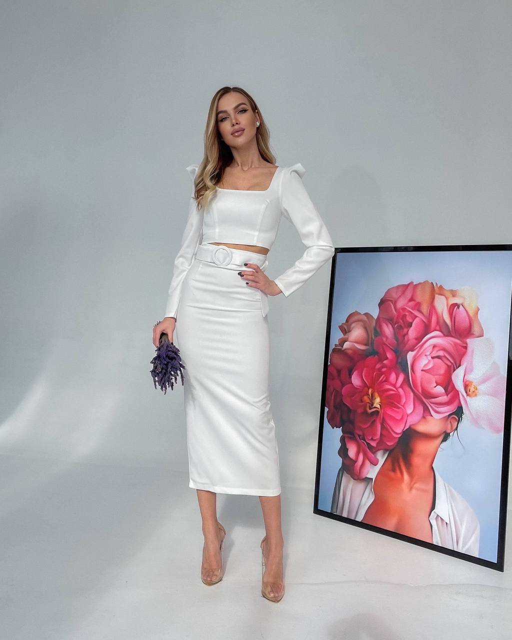 Woman in a white outfit standing next to a painting of flowers on a gray background