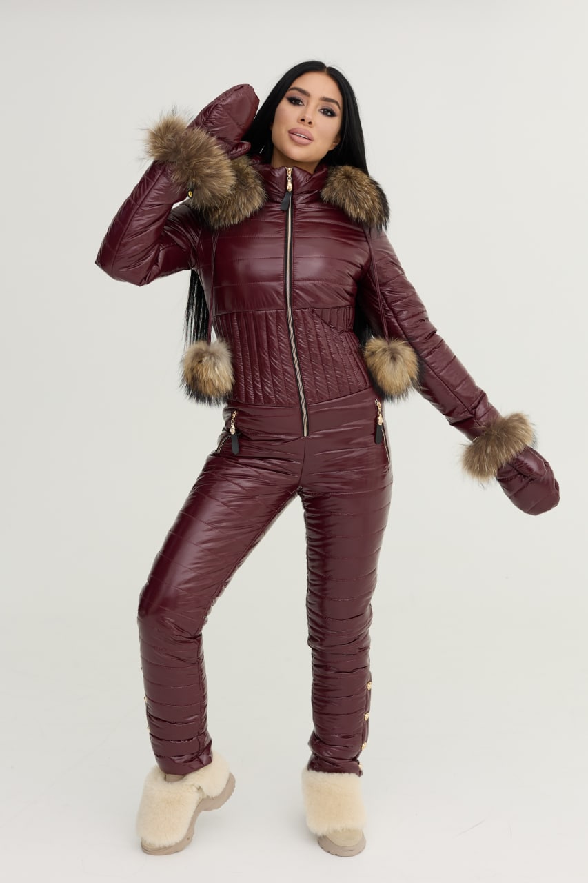 Person wearing a maroon puffer jumpsuit with fur trim on a white background