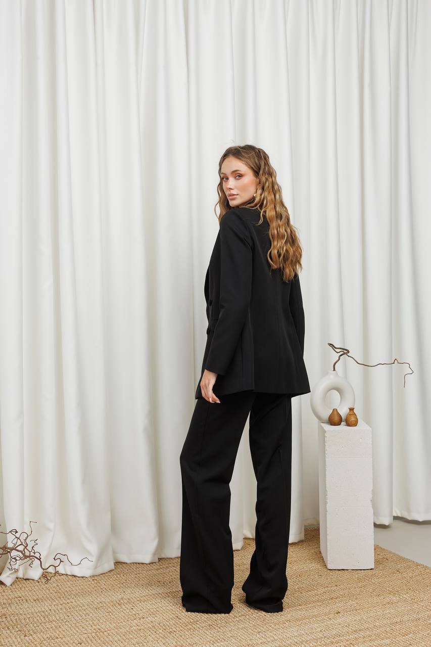 Woman in a black suit standing in front of white curtains