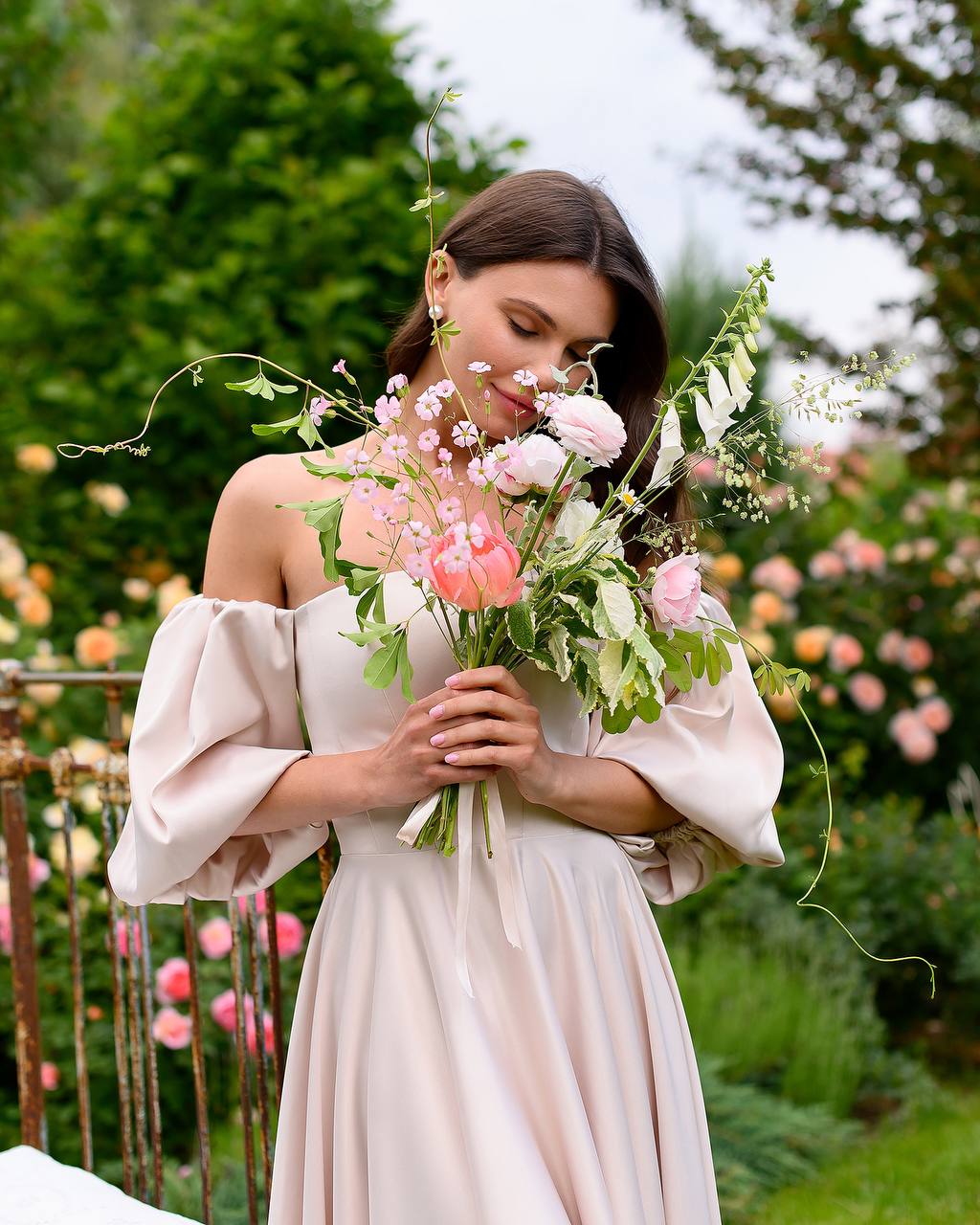 Woman in a light pink dress holding a bouquet of flowers in a garden setting