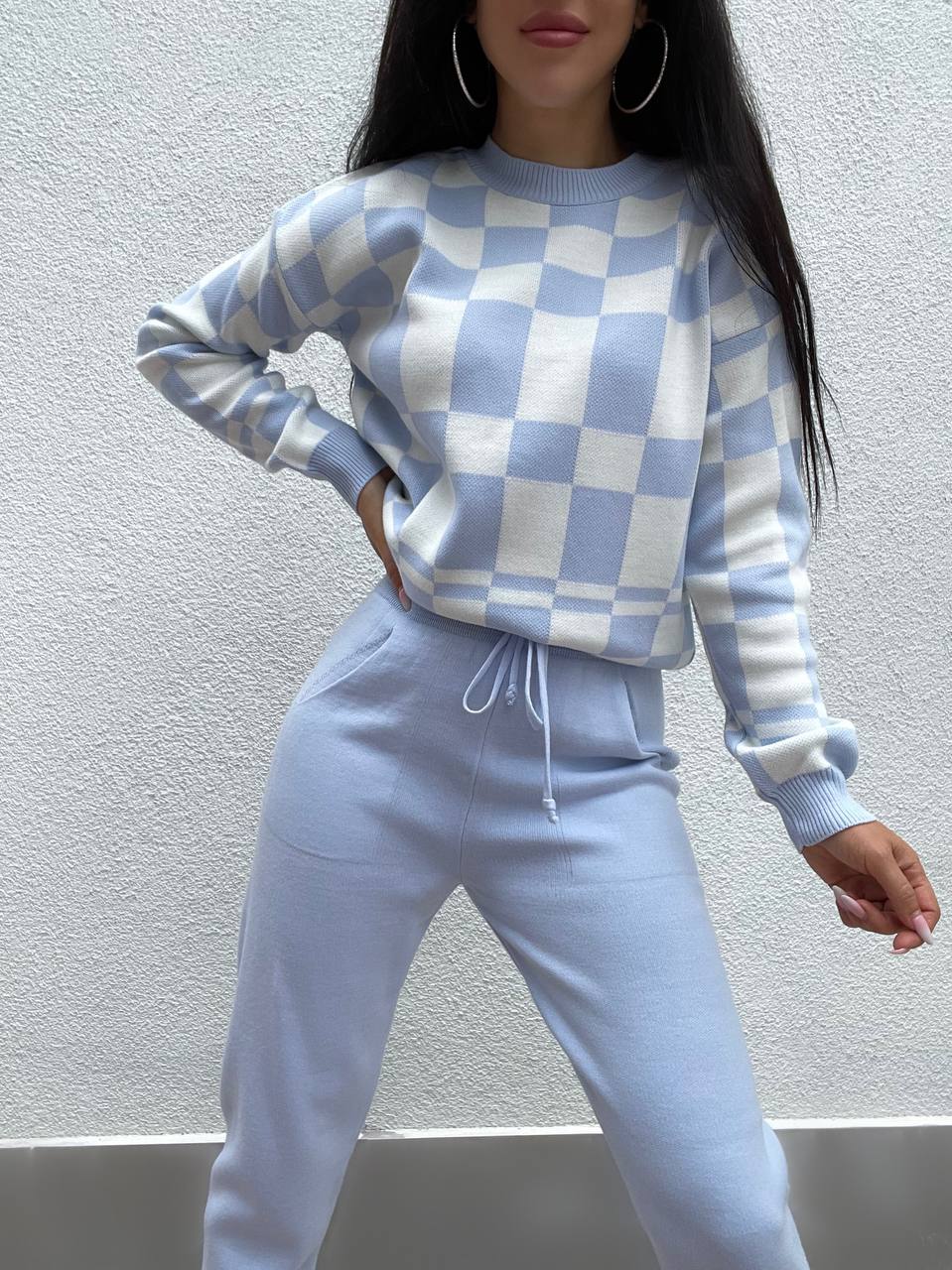 Person wearing a blue and white checkered sweater and pants against a plain background