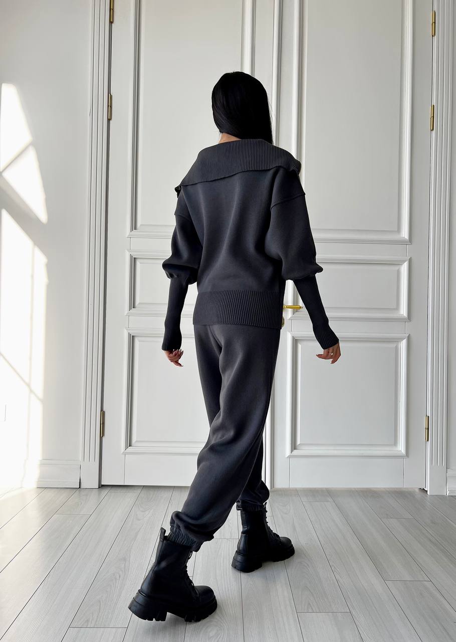 Person wearing a dark outfit in a room with white walls and wooden floor.
