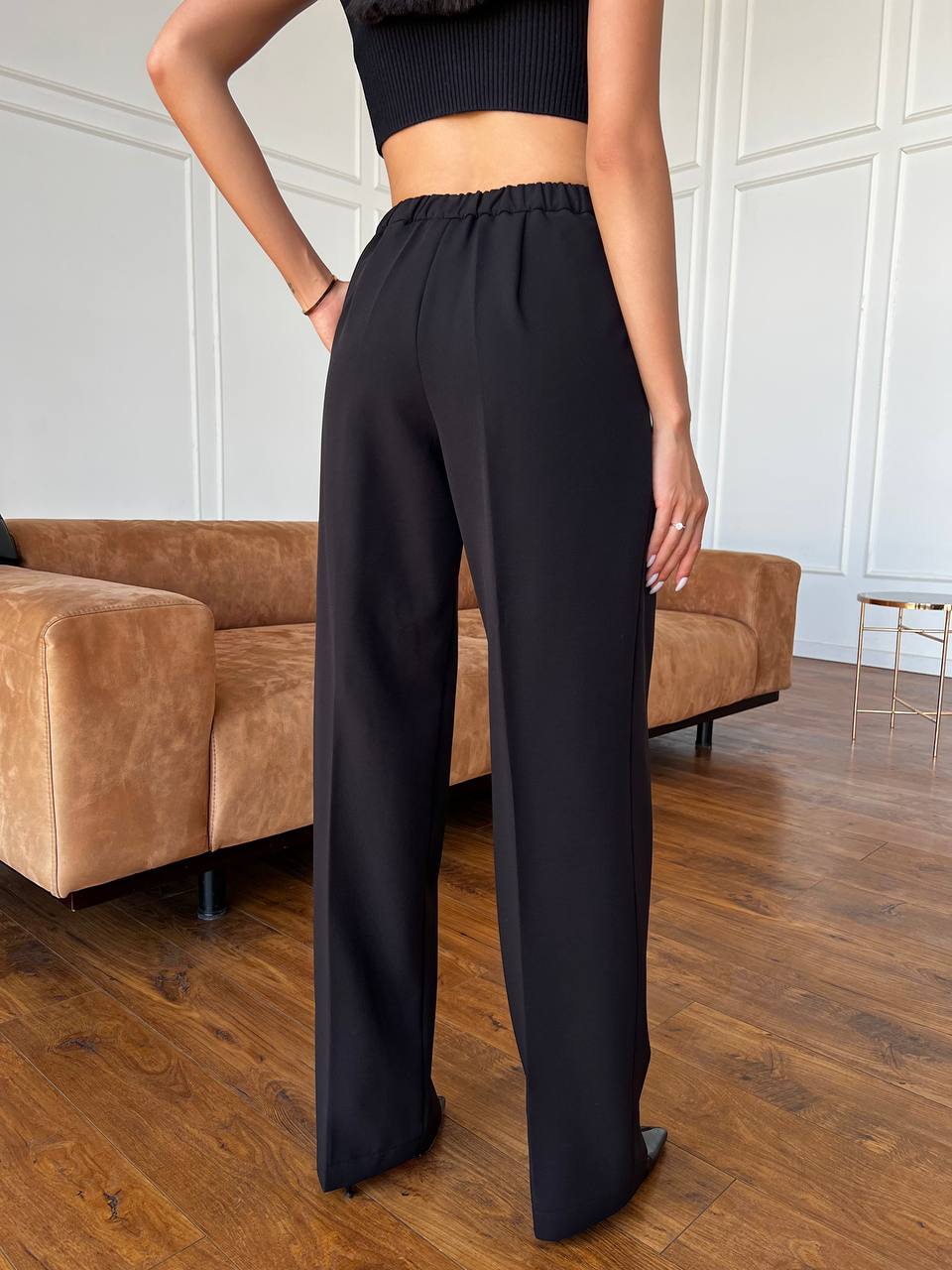 Person wearing black high-waisted pants standing in a room with a brown sofa.