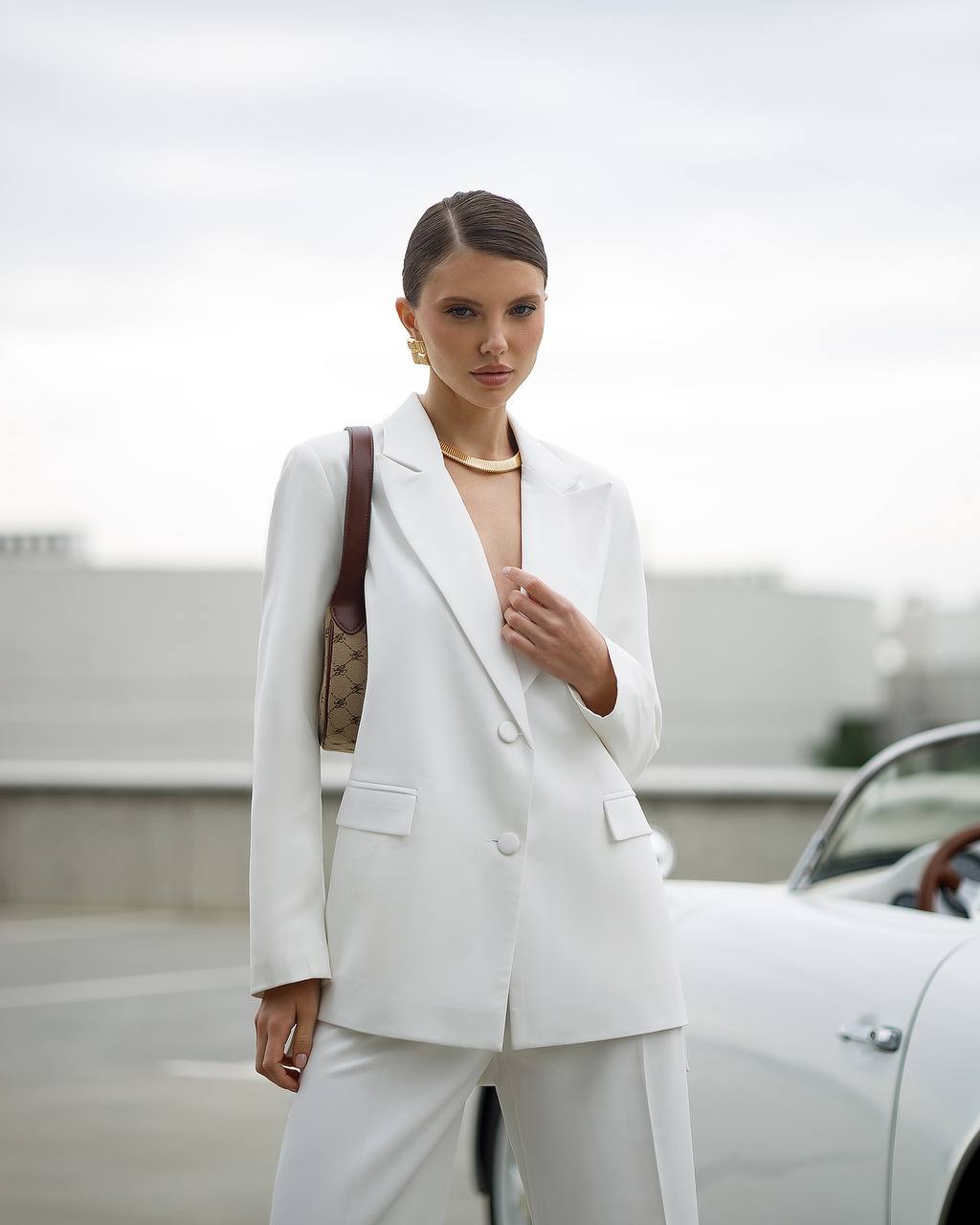 Woman in a white suit standing next to a car with a blurred background