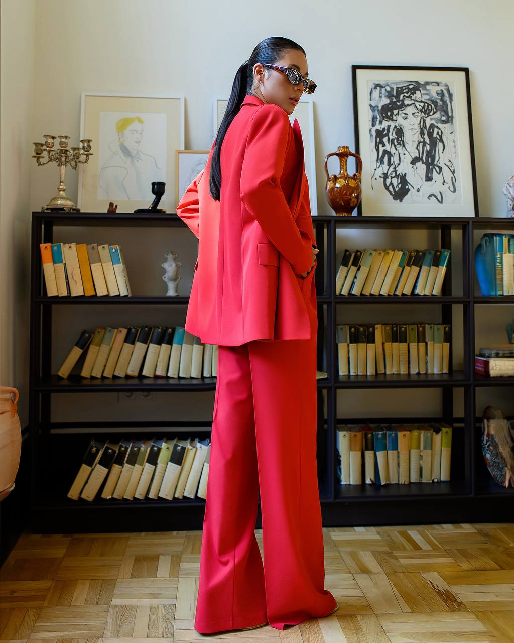 Person wearing a red suit standing in a room with bookshelves and artwork.