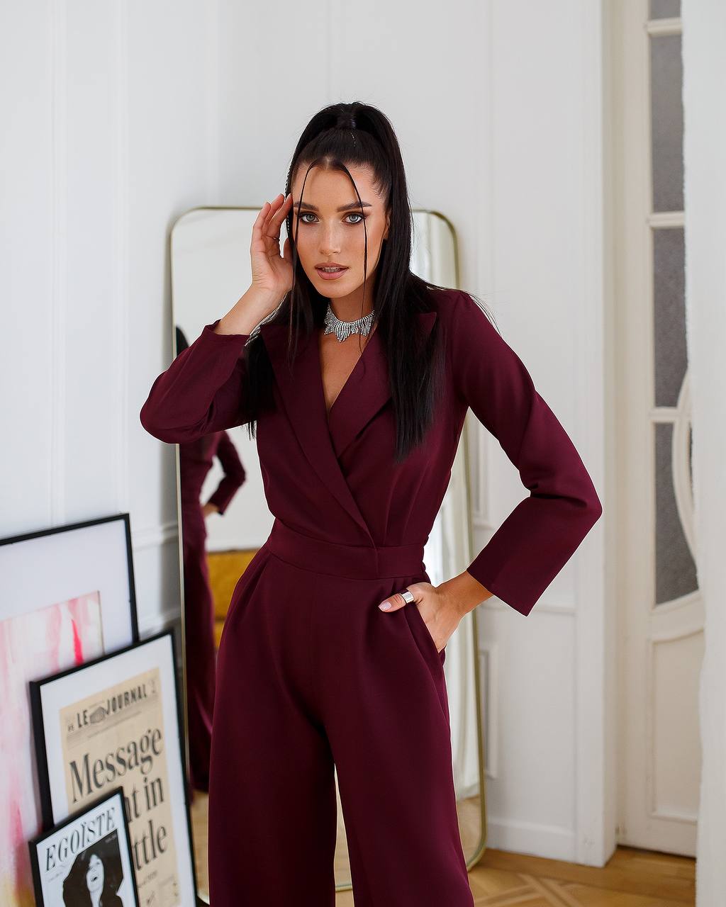 Woman in a burgundy jumpsuit standing in a room with framed pictures on the wall.