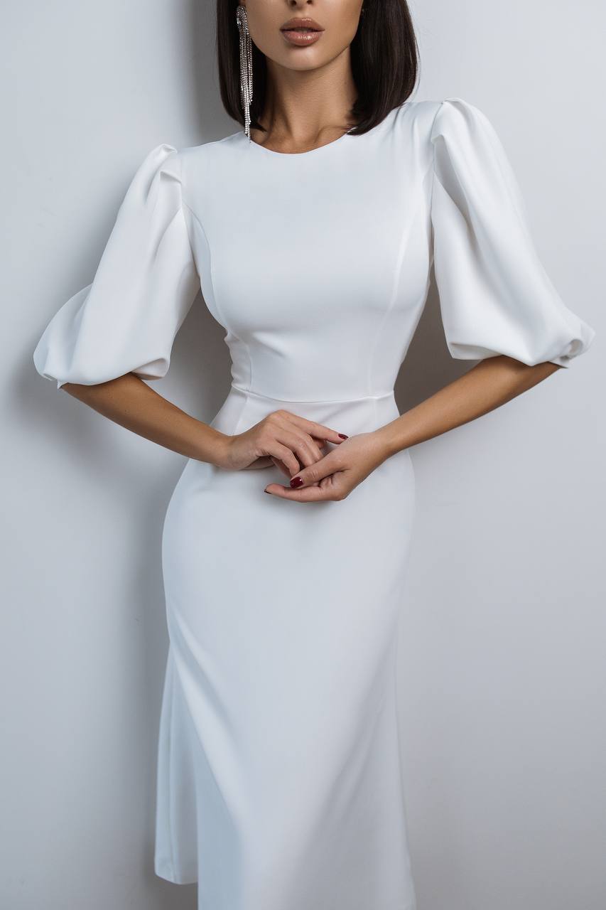 Woman wearing a white dress with puffed sleeves against a plain background