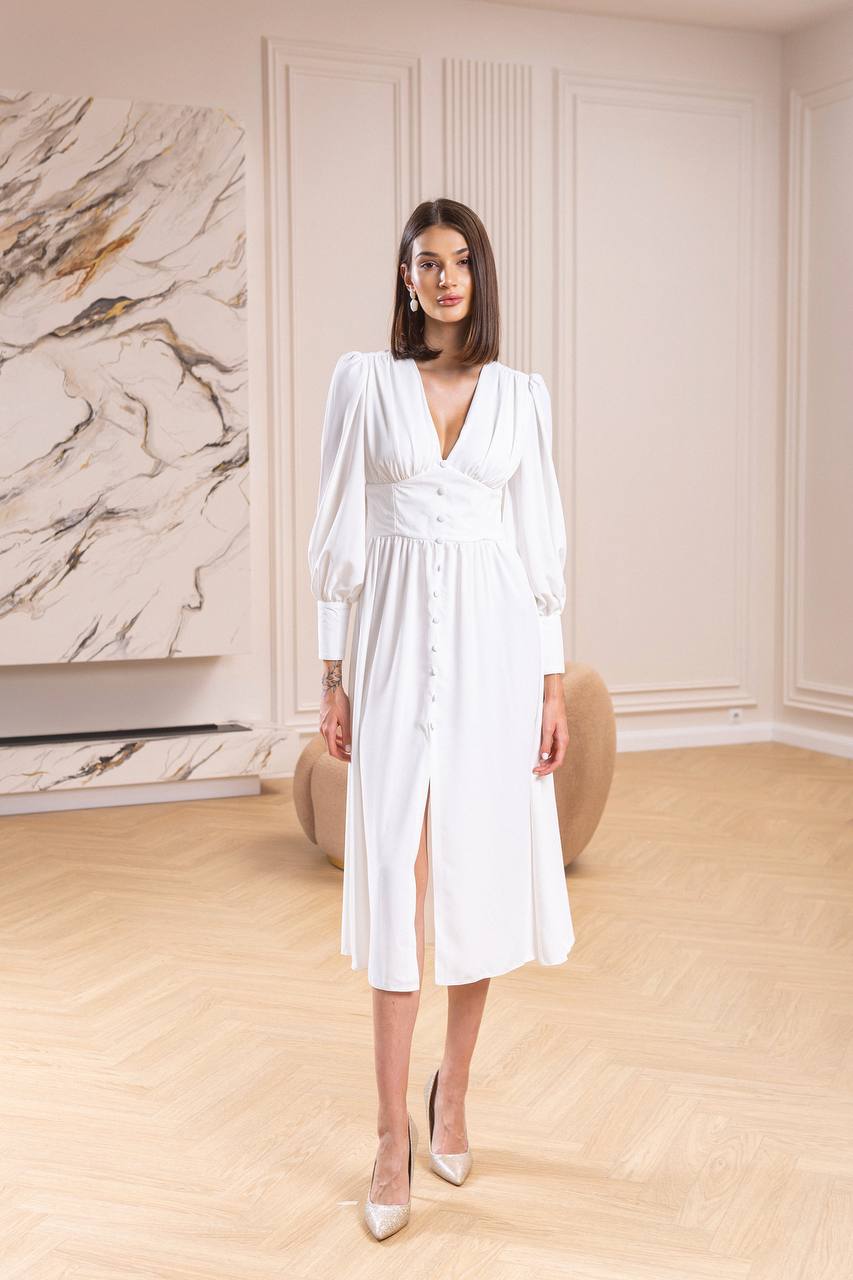Woman in a white dress standing in a room with marble wall and wooden floor.