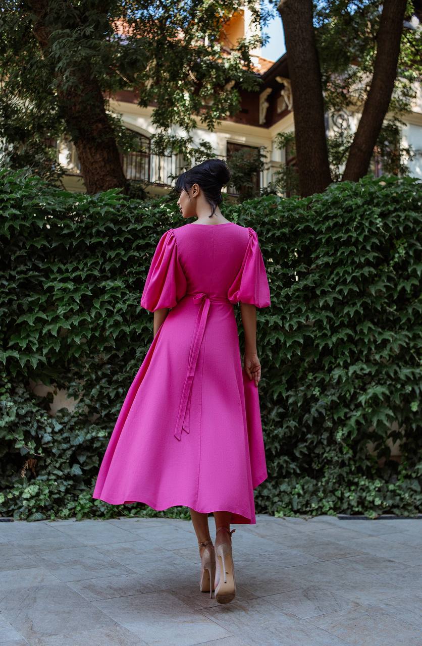 Woman in a bright pink dress standing outdoors with greenery in the background