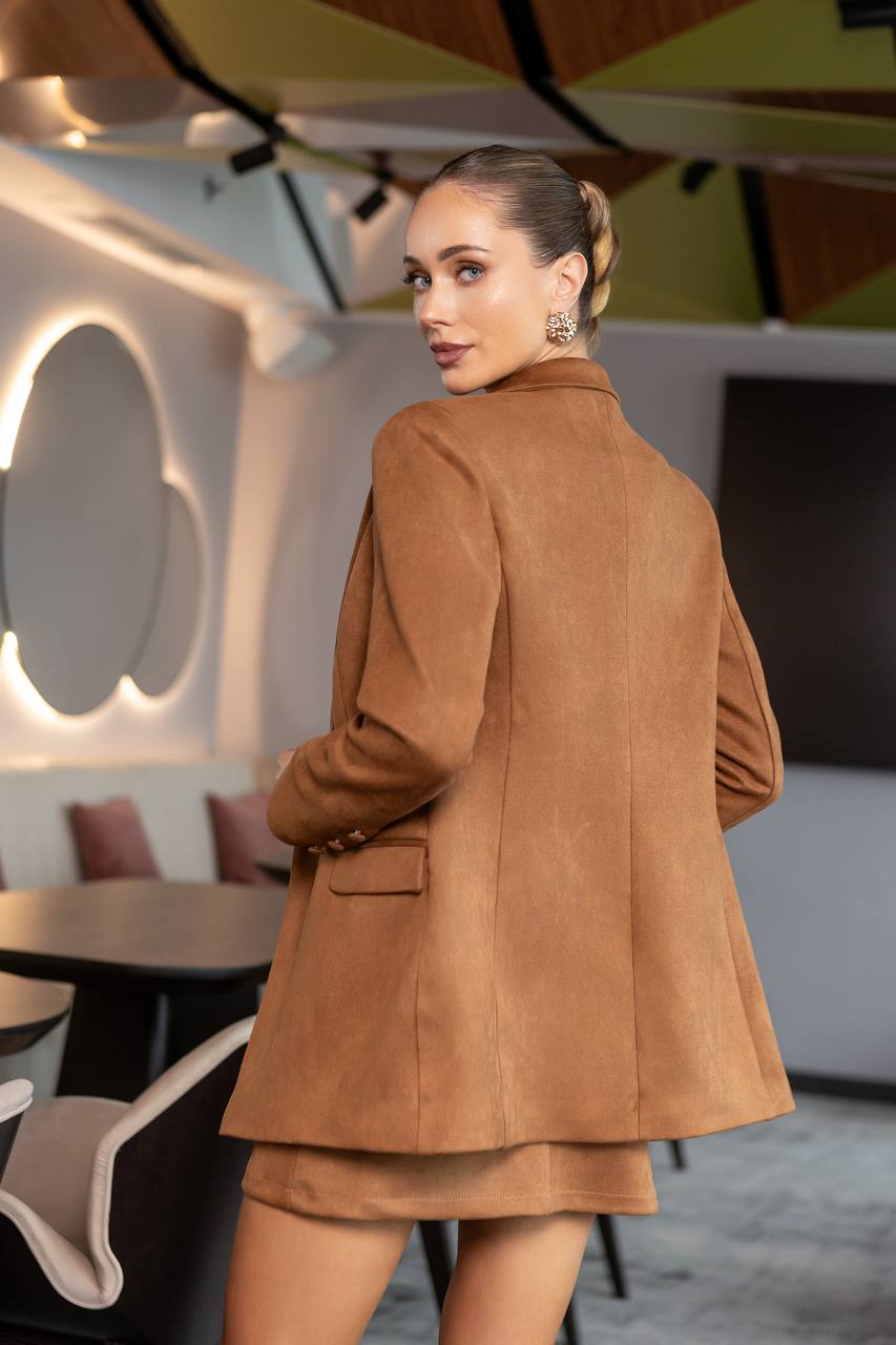 Woman in a brown coat standing in an indoor setting with modern decor.