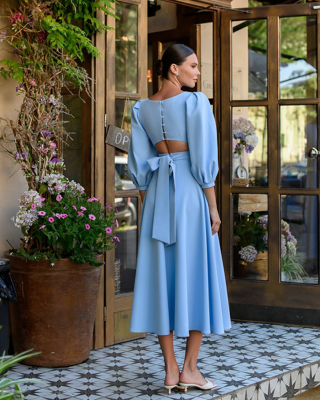 Woman in a light blue dress standing in front of a store entrance with flowers.