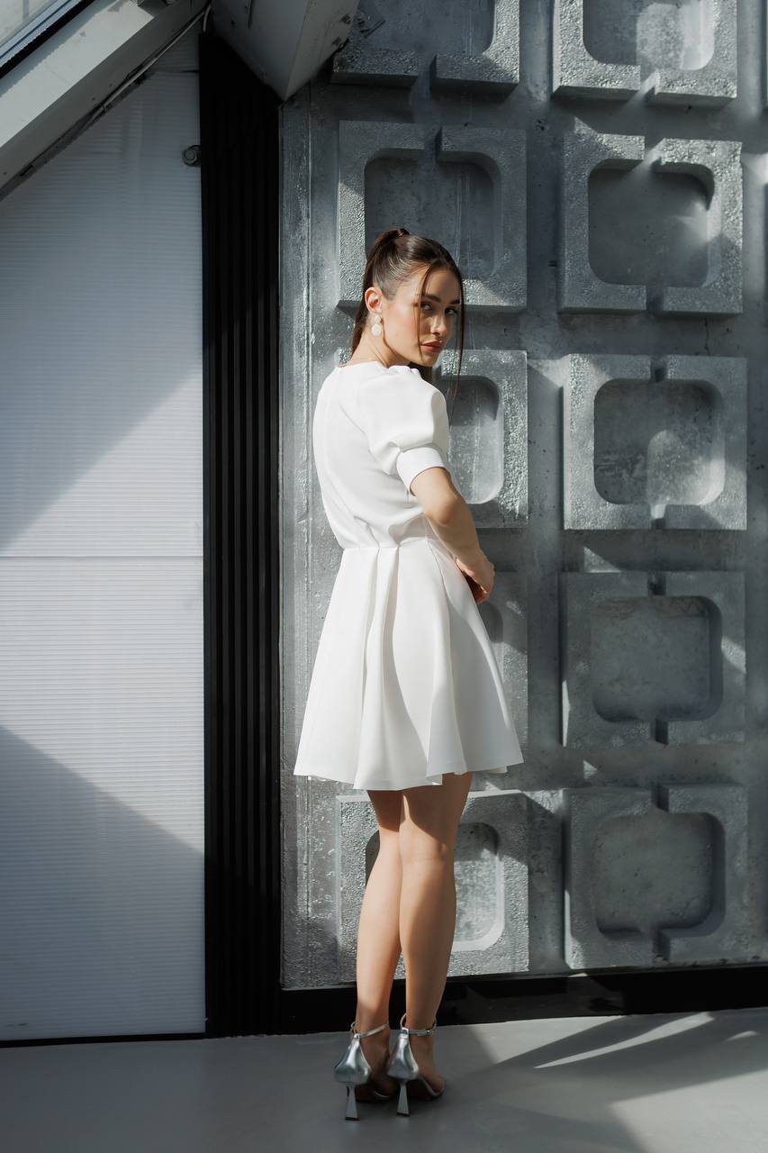 Woman in a white dress standing against a textured wall.
