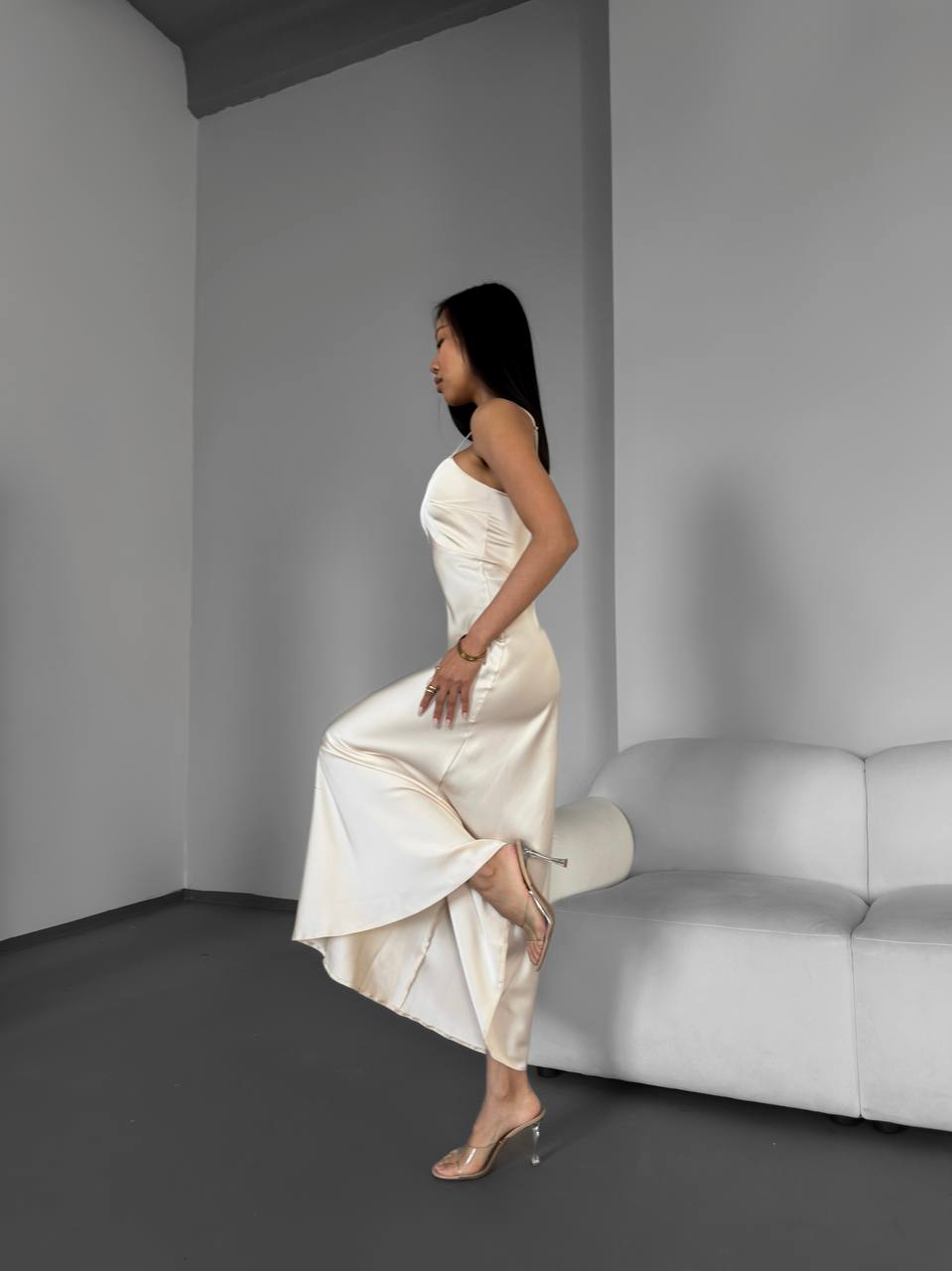 Woman in a white dress sitting on a white couch in a minimalistic room.