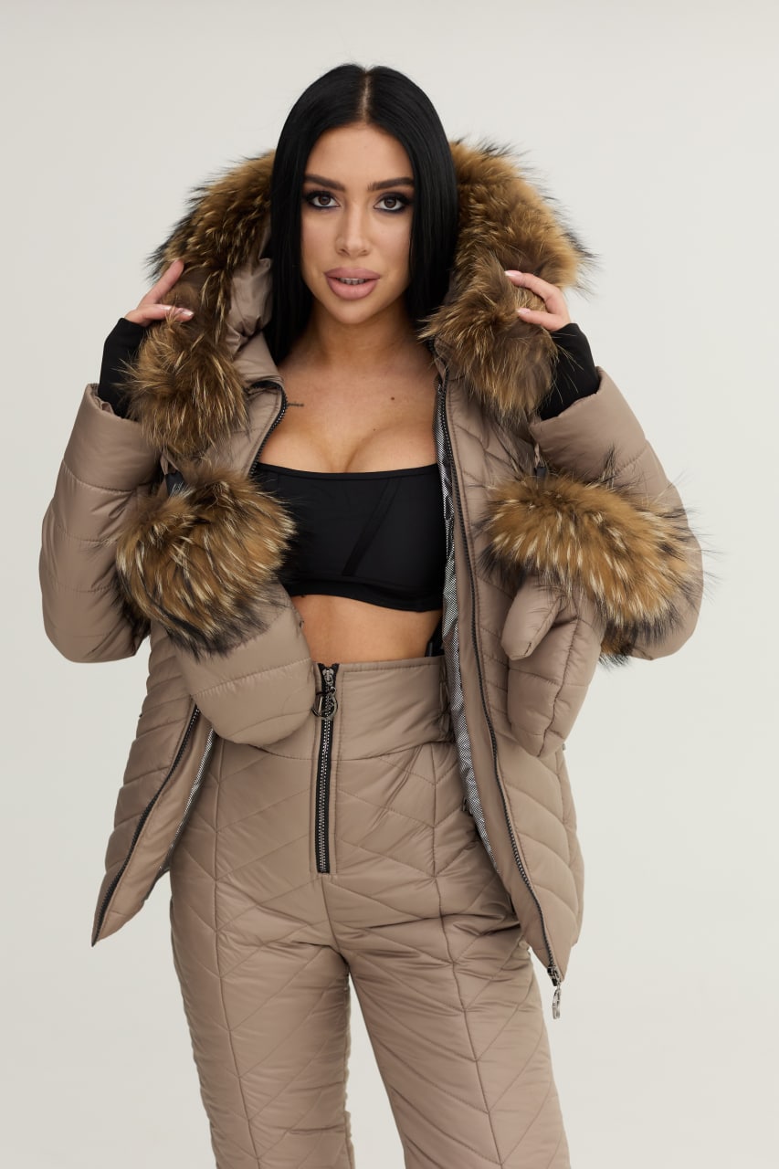 Woman wearing a beige puffer jacket with fur hood on a plain background
