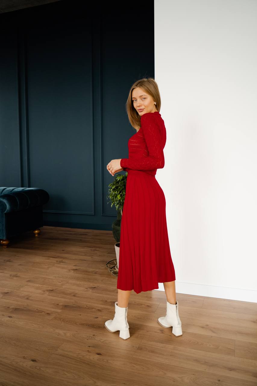 Woman in a red dress standing in a room with dark blue walls and wooden floor.