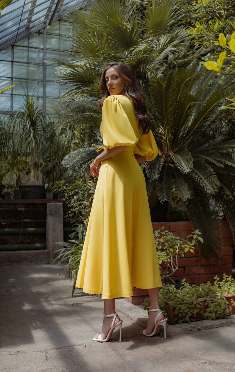 Woman in a yellow dress standing in a greenhouse with plants around