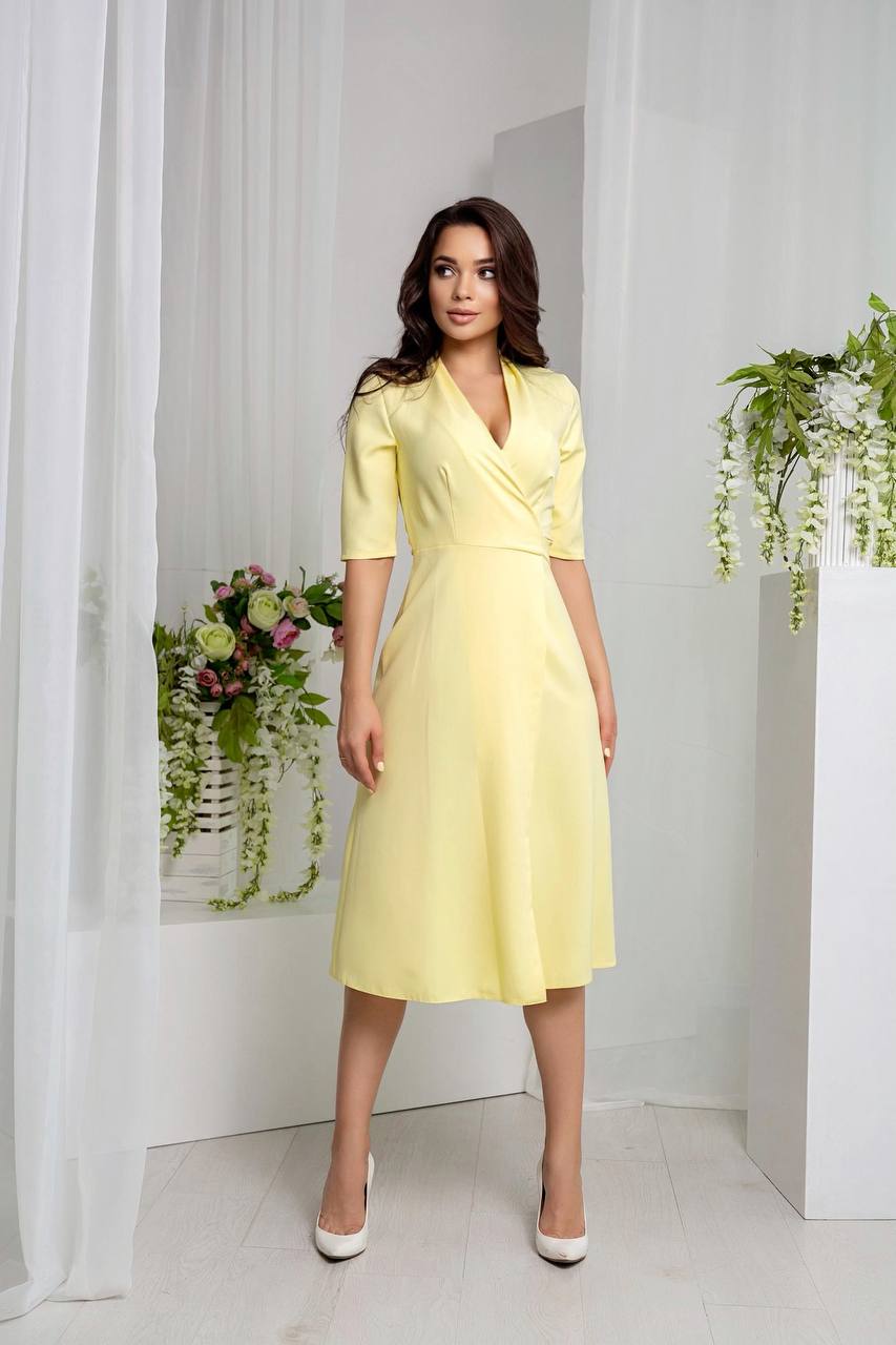 Woman wearing a yellow dress standing in a bright room with white walls and plants.