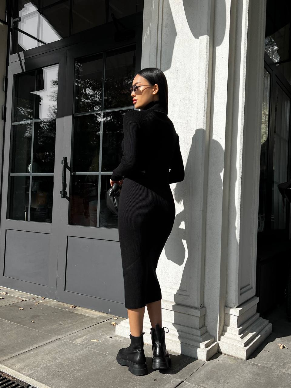 Person wearing a black outfit standing against a building with columns.