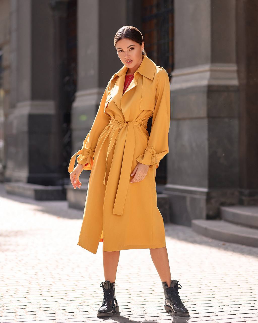 Woman wearing a yellow trench coat standing on a city street.