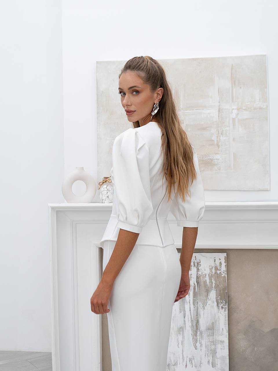 Woman in a white outfit standing in a minimalistic room with abstract art on the wall.