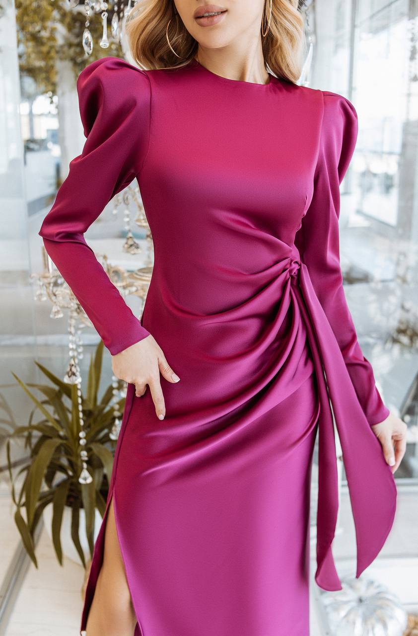 Woman wearing a magenta dress with long sleeves and a front knot detail, standing indoors.