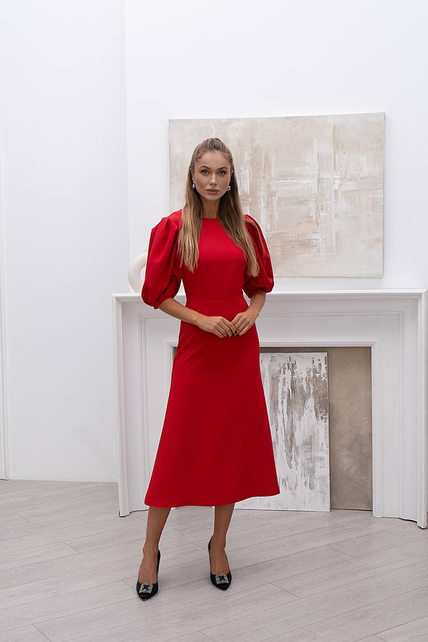 Woman in a red dress standing in a room with white walls and a fireplace.