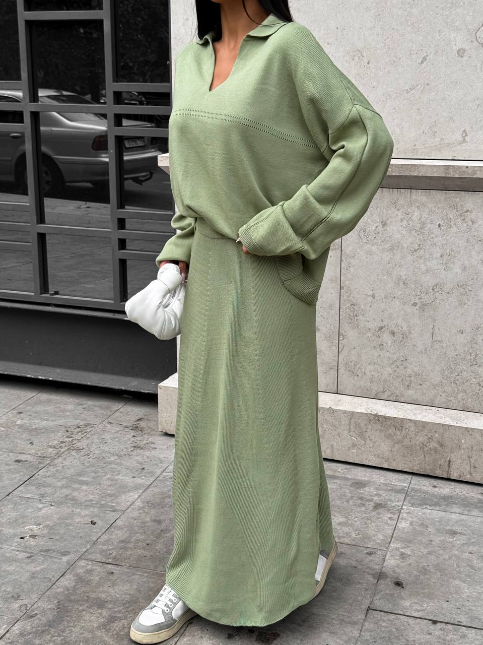 Person wearing a long green dress with white sneakers on a city street.