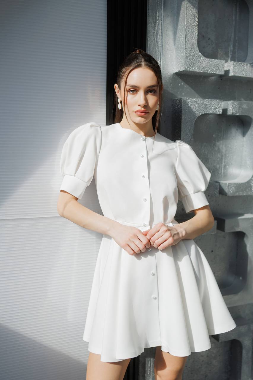 Woman wearing a white dress standing against a textured wall.