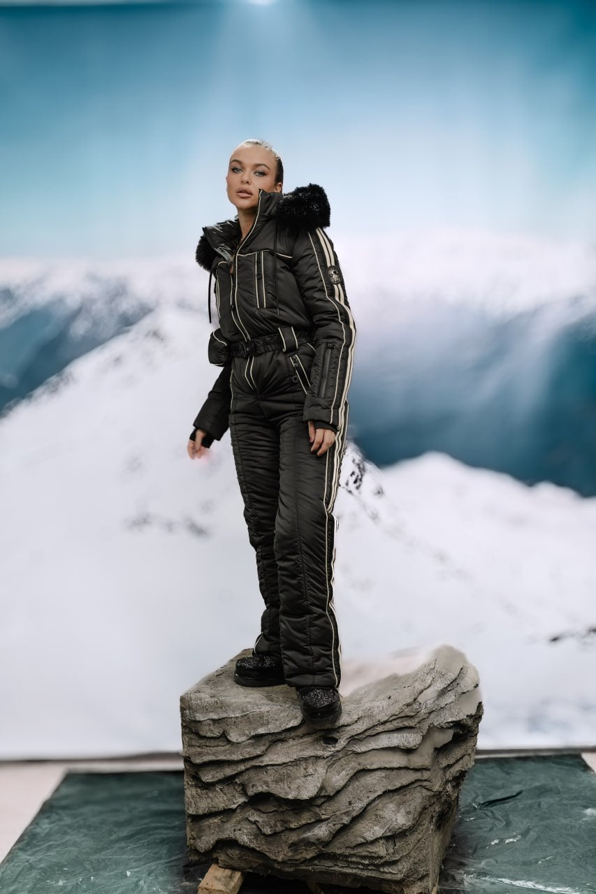 Person in a black winter outfit standing on a rock with a mountainous background