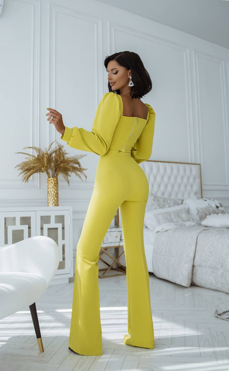 Woman in a yellow jumpsuit standing in a stylish room with white walls and decor.