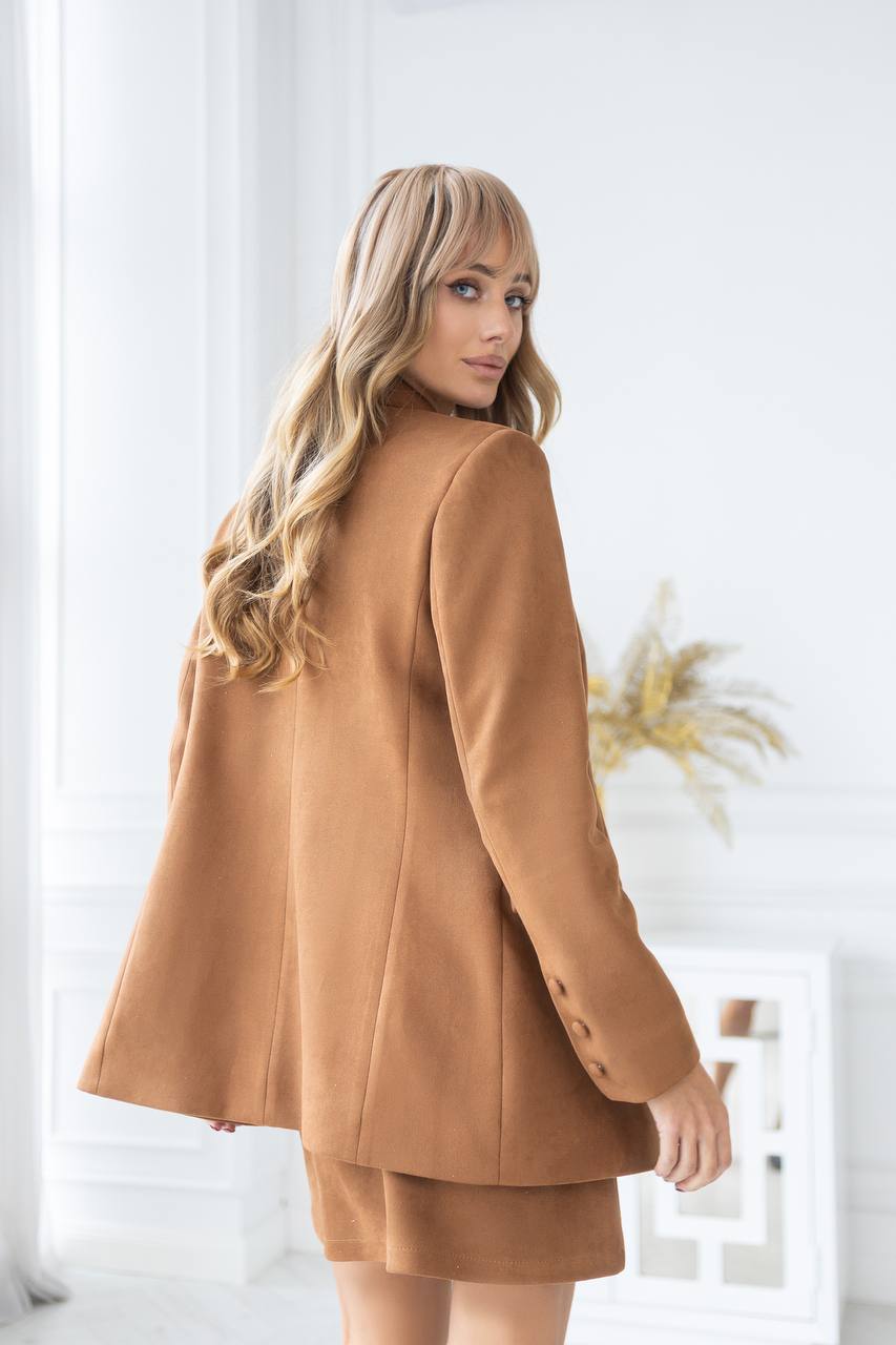 Woman wearing a brown coat in a bright room with white curtains.