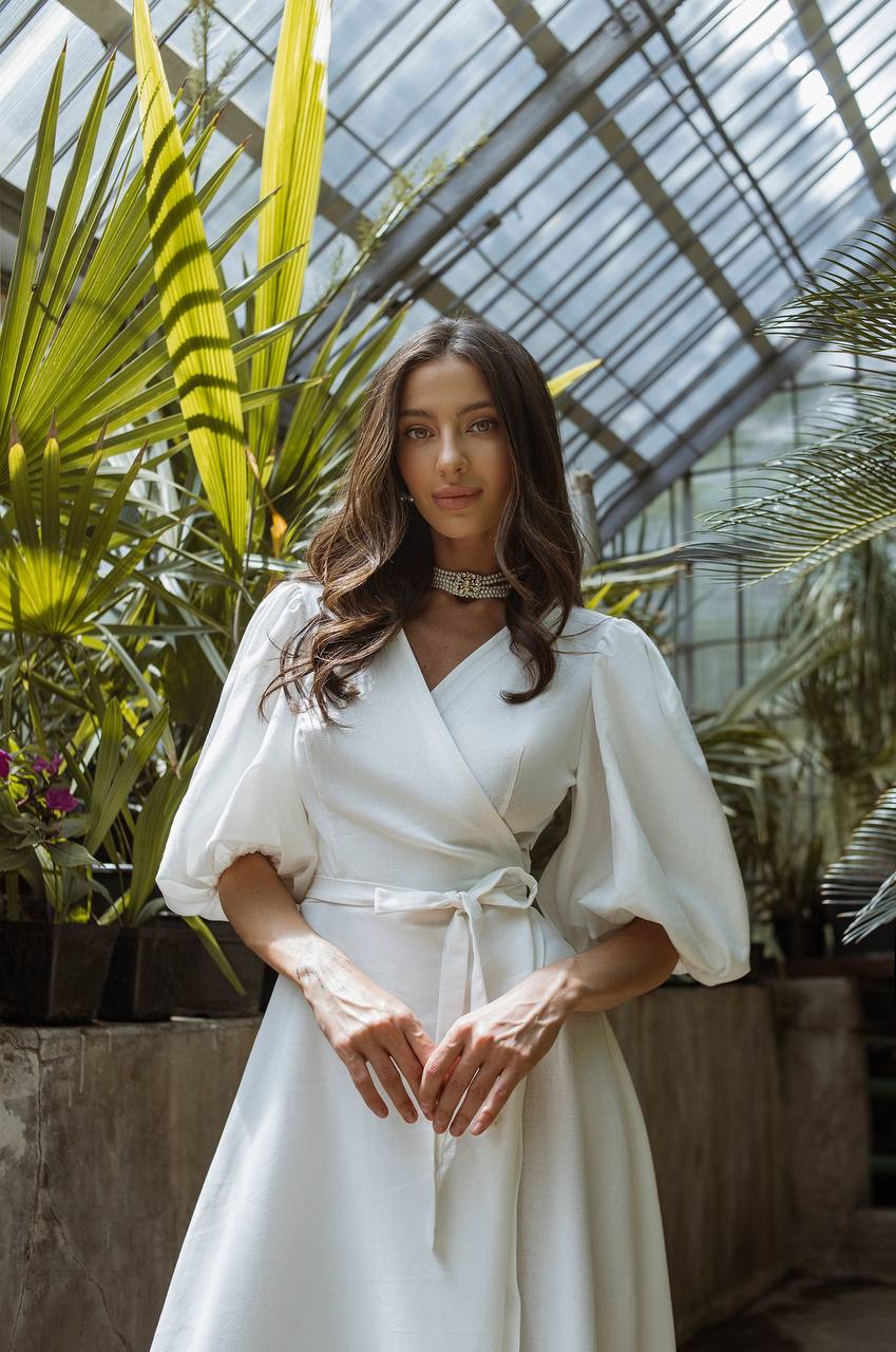 Woman in a white dress standing in a greenhouse with plants around