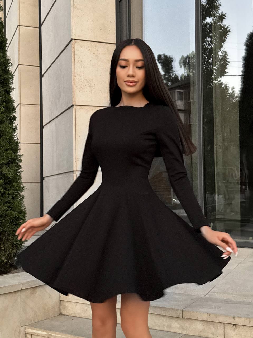 Woman wearing a black dress standing outdoors near a building.